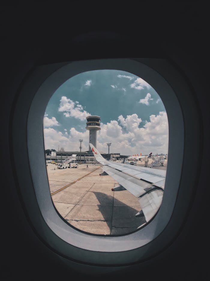 Airplane wing view through window showing airport control tower and tarmac.